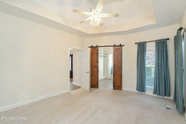 unfurnished room featuring a tray ceiling, light colored carpet, a barn door, and ceiling fan