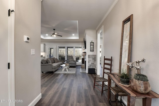 living room featuring dark wood-type flooring, ornamental molding, a raised ceiling, ceiling fan, and a fireplace