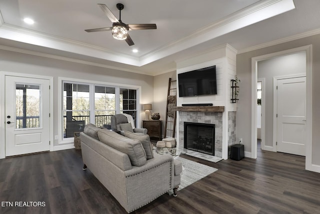 living room with dark wood-type flooring, crown molding, a tray ceiling, ceiling fan, and a fireplace