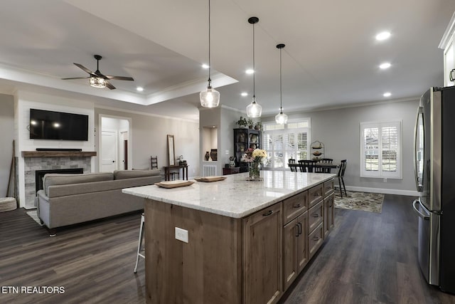 kitchen featuring pendant lighting, stainless steel refrigerator, dark hardwood / wood-style floors, light stone countertops, and a kitchen island