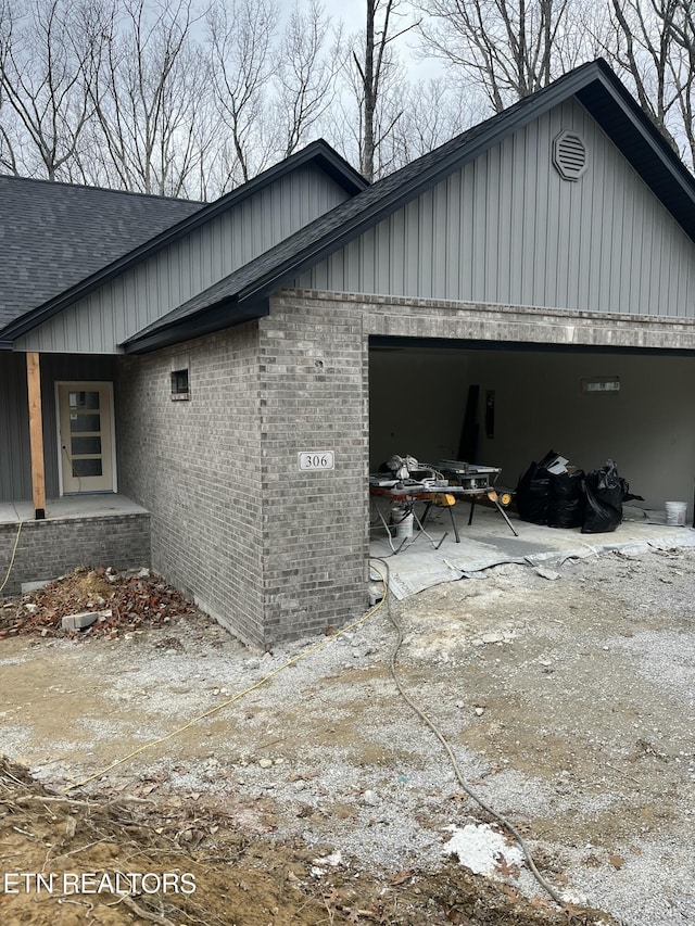 view of property exterior with brick siding, an attached garage, and roof with shingles