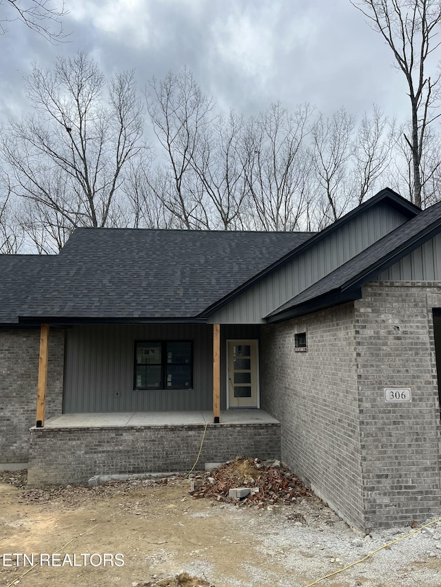 view of front facade featuring board and batten siding, brick siding, and roof with shingles