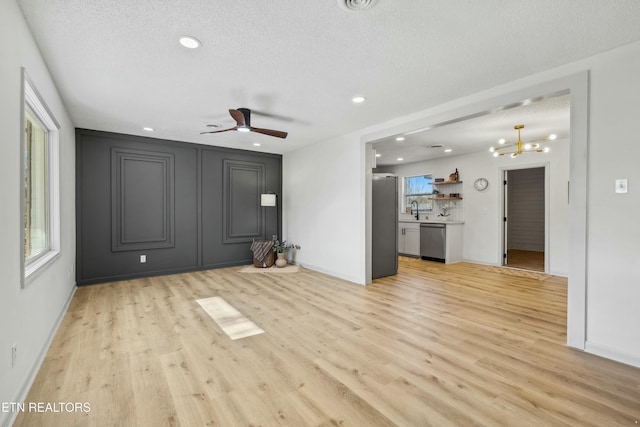 unfurnished living room featuring sink, ceiling fan with notable chandelier, a textured ceiling, and light wood-type flooring