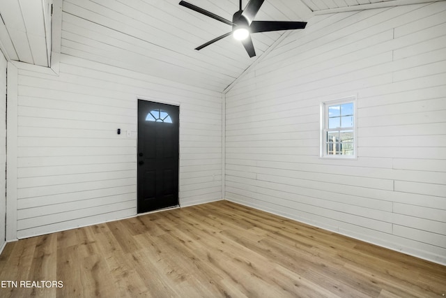 entryway with ceiling fan, wood walls, vaulted ceiling, and light wood-type flooring