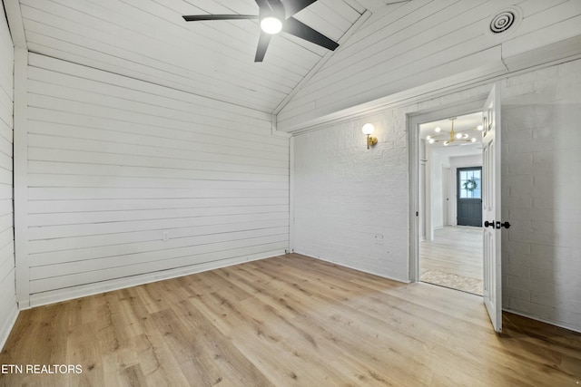 empty room featuring ceiling fan, vaulted ceiling, brick wall, and light wood-type flooring