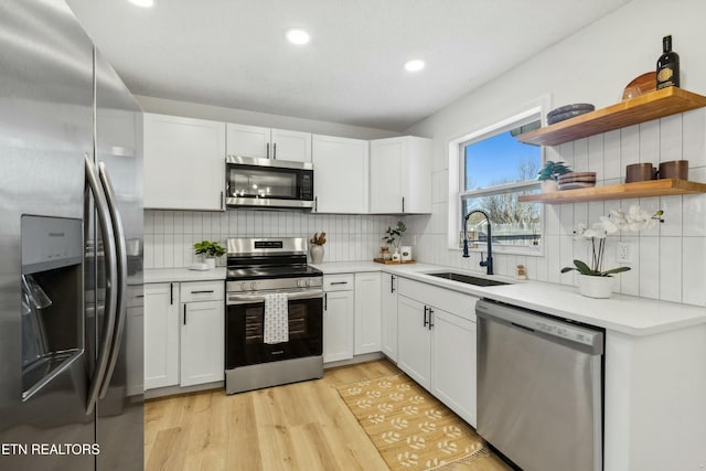 kitchen featuring sink, white cabinetry, appliances with stainless steel finishes, light hardwood / wood-style floors, and decorative backsplash