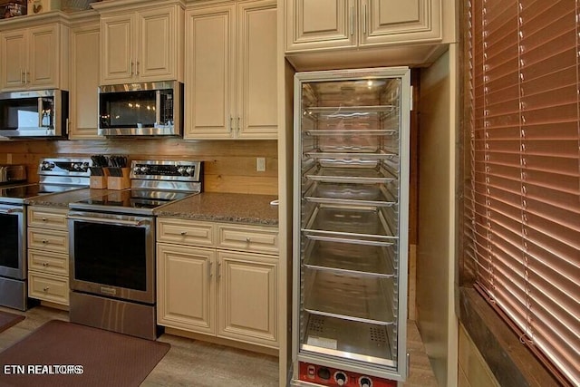 kitchen with appliances with stainless steel finishes, stone countertops, beverage cooler, and cream cabinetry