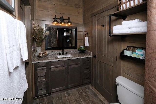 bathroom with vanity, wooden walls, and toilet