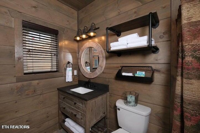 bathroom featuring toilet, vanity, and wood walls