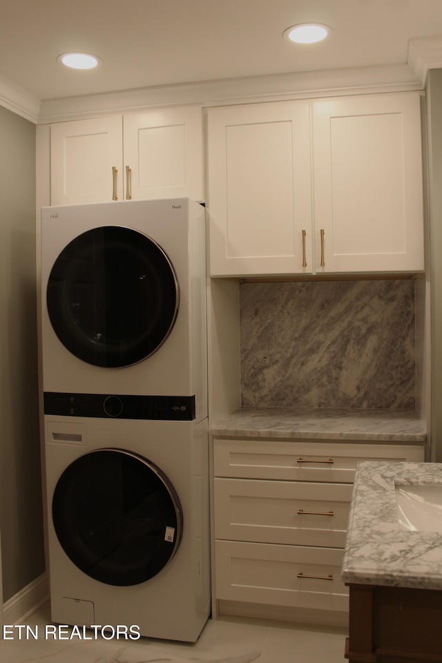 laundry area with cabinets, stacked washer / drying machine, and ornamental molding