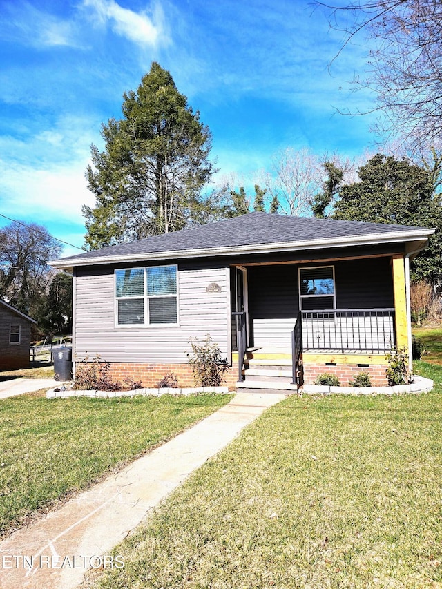 single story home featuring covered porch, a shingled roof, and a front yard