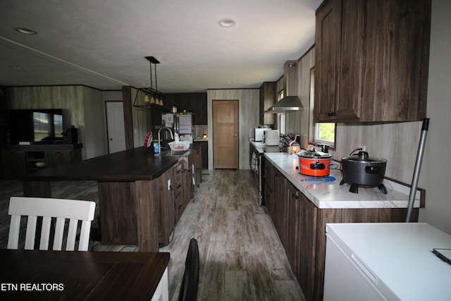 kitchen featuring stainless steel range with electric cooktop, dark brown cabinets, light hardwood / wood-style flooring, an island with sink, and pendant lighting