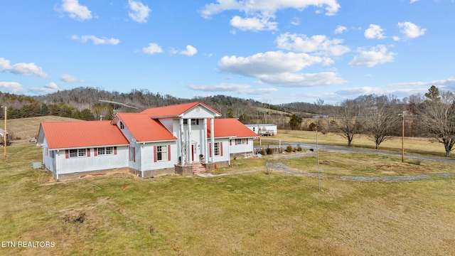 view of front of property with metal roof, a view of trees, and a front lawn