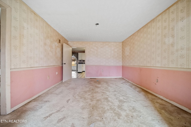 unfurnished room with carpet floors, wallpapered walls, baseboards, and wainscoting