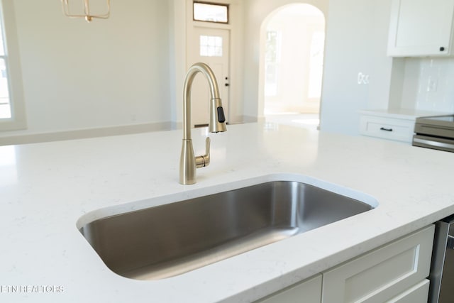 room details featuring tasteful backsplash, sink, light stone countertops, and white cabinets