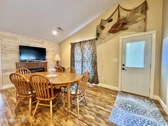 dining area with wood-type flooring, lofted ceiling, and wood walls