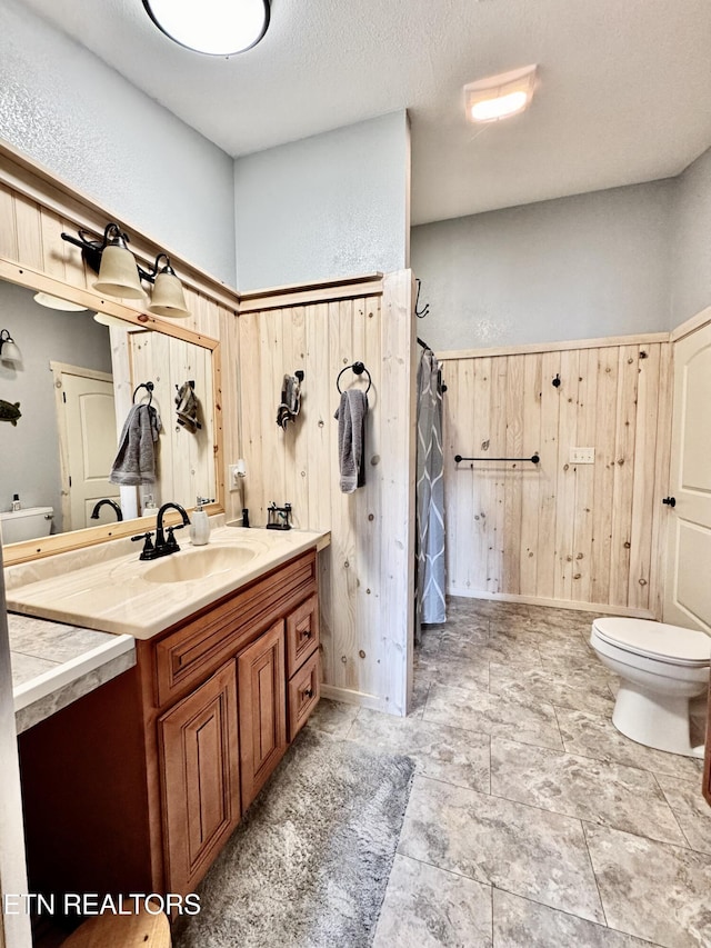 bathroom with vanity, a textured ceiling, wooden walls, and toilet