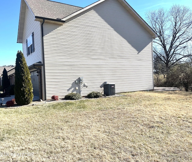 view of side of home with a garage, a yard, and central AC