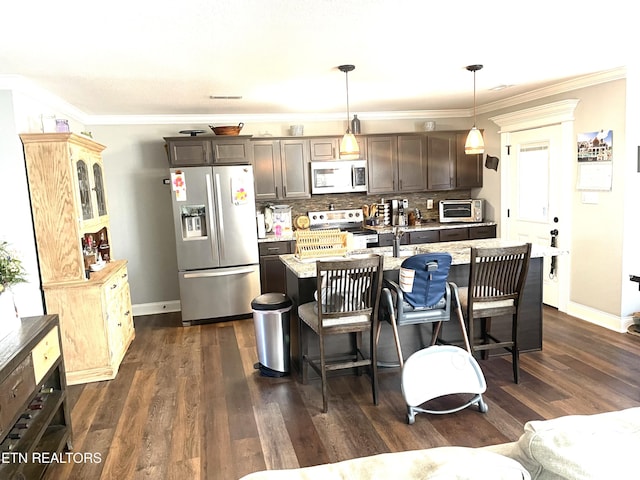 kitchen with appliances with stainless steel finishes, decorative light fixtures, an island with sink, dark brown cabinetry, and light stone counters