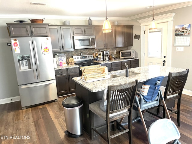 kitchen with a kitchen bar, hanging light fixtures, a center island with sink, appliances with stainless steel finishes, and dark hardwood / wood-style floors