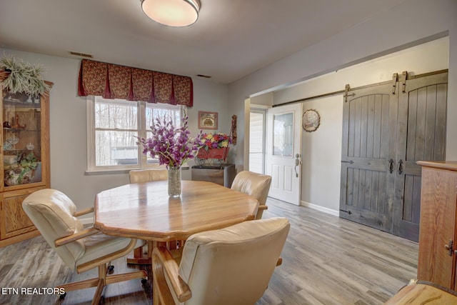 dining room with a barn door and light hardwood / wood-style flooring