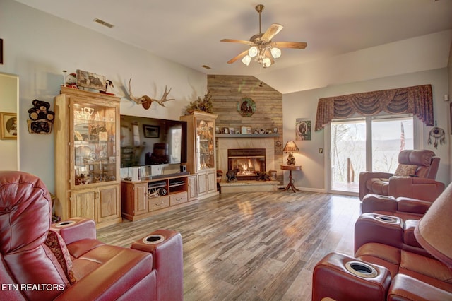 living room with ceiling fan, a fireplace, vaulted ceiling, and light wood-type flooring