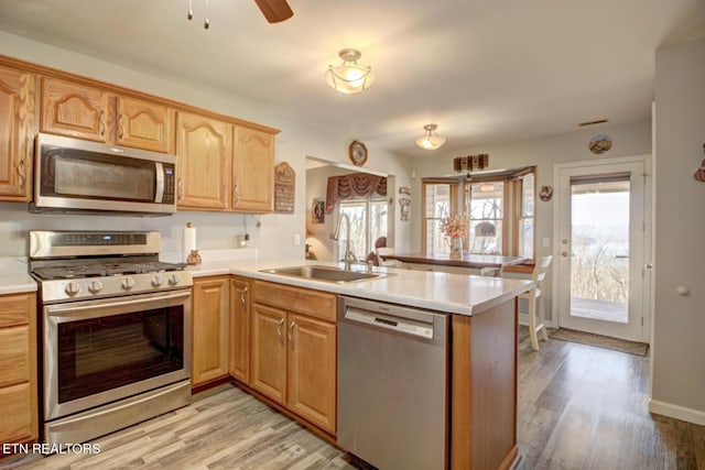 kitchen with stainless steel appliances, sink, kitchen peninsula, a healthy amount of sunlight, and light hardwood / wood-style floors