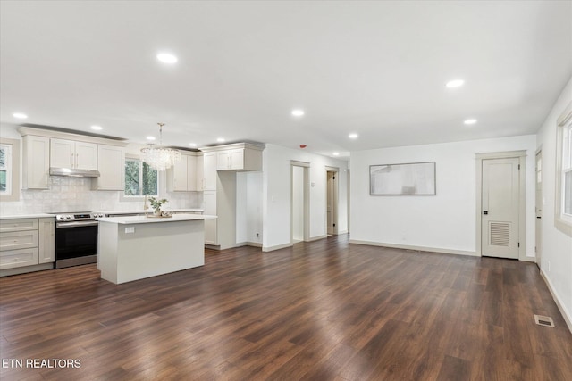 kitchen featuring stainless steel electric range oven, a kitchen island, backsplash, hanging light fixtures, and dark wood-type flooring