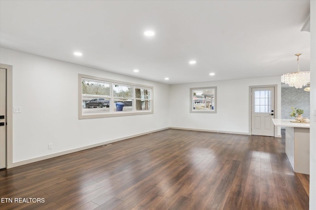 unfurnished living room with an inviting chandelier and dark hardwood / wood-style floors