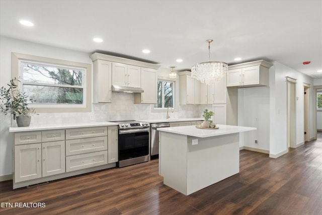 kitchen featuring dark wood-type flooring, a center island, hanging light fixtures, appliances with stainless steel finishes, and backsplash