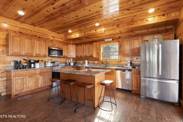 kitchen featuring stainless steel appliances, a center island, light stone counters, a kitchen bar, and dark hardwood / wood-style flooring