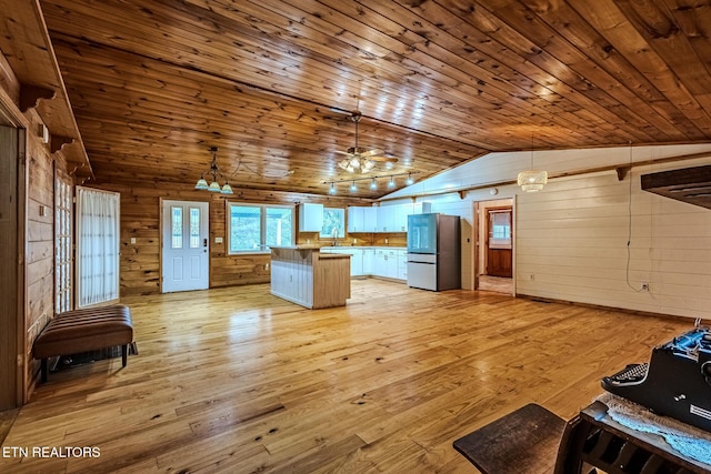 interior space featuring vaulted ceiling, stainless steel refrigerator, decorative light fixtures, wooden ceiling, and light hardwood / wood-style flooring