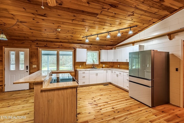 kitchen with lofted ceiling, stainless steel refrigerator, white cabinets, and wood walls