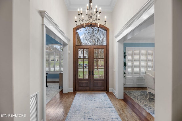 foyer featuring light wood-type flooring, a high ceiling, crown molding, an inviting chandelier, and french doors