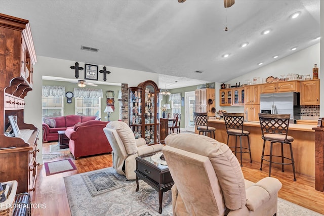 living room featuring lofted ceiling, a textured ceiling, light hardwood / wood-style flooring, and ceiling fan