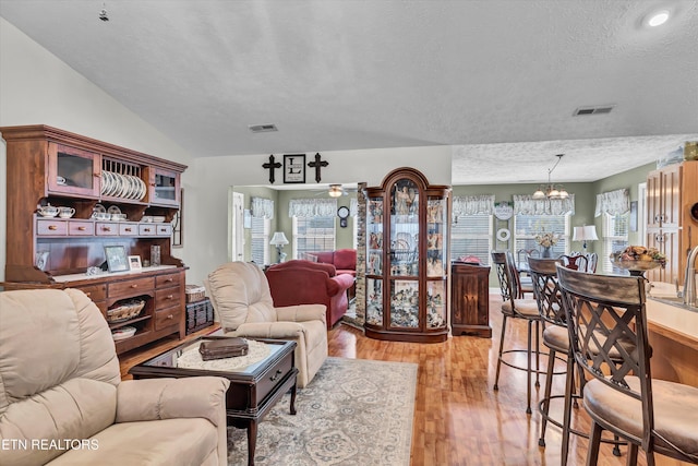 living room featuring lofted ceiling, ceiling fan with notable chandelier, a textured ceiling, and light wood-type flooring