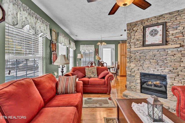 living room featuring ceiling fan, a stone fireplace, a textured ceiling, and light hardwood / wood-style floors