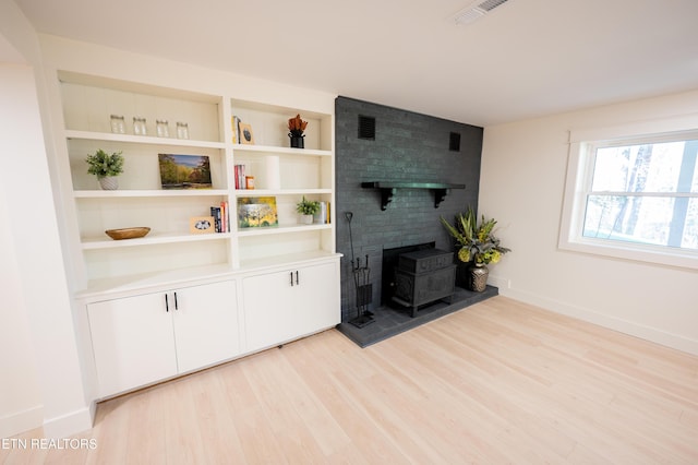 living room with built in shelves, light hardwood / wood-style floors, and a wood stove