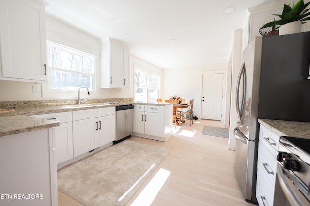 kitchen with appliances with stainless steel finishes, sink, white cabinets, light stone counters, and light wood-type flooring