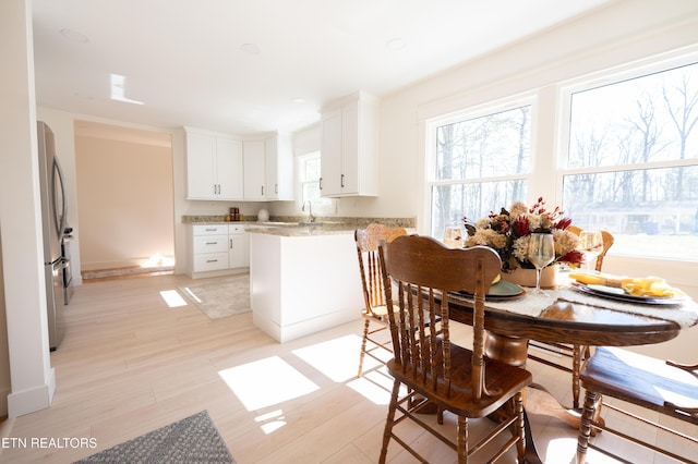 kitchen featuring light stone countertops, white cabinets, stainless steel refrigerator, and light hardwood / wood-style floors