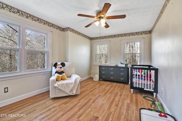 bedroom with ceiling fan, a nursery area, and light hardwood / wood-style floors