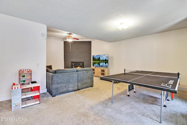 recreation room featuring a brick fireplace, ceiling fan, and carpet flooring