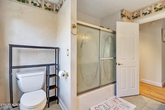 bathroom featuring combined bath / shower with glass door, tile patterned floors, and toilet