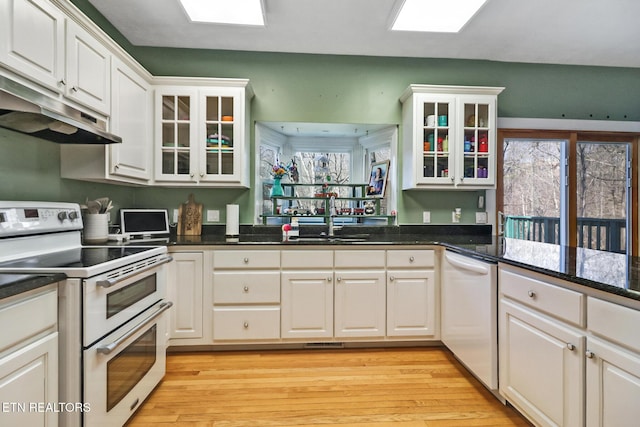 kitchen with sink, white appliances, white cabinetry, light hardwood / wood-style floors, and dark stone counters