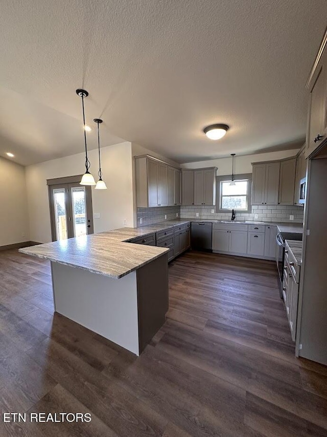 kitchen with dark wood-type flooring, hanging light fixtures, stainless steel appliances, tasteful backsplash, and kitchen peninsula