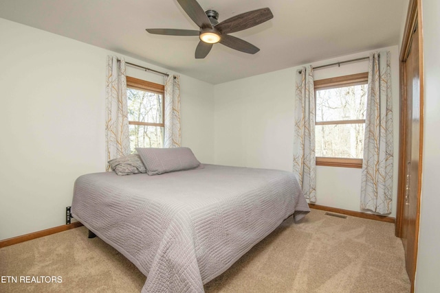 bedroom featuring multiple windows, light colored carpet, ceiling fan, and a closet