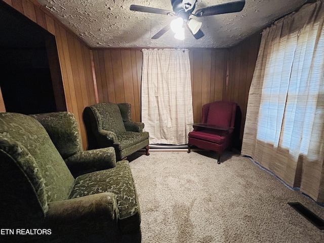 living area with carpet flooring, ceiling fan, a textured ceiling, and wood walls