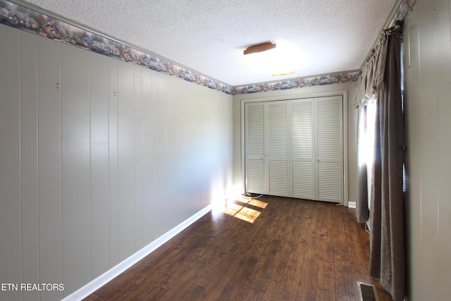 unfurnished bedroom featuring a textured ceiling, dark wood-style flooring, visible vents, baseboards, and a closet