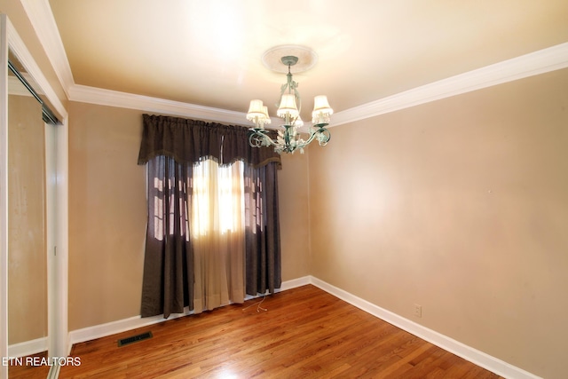 spare room featuring wood finished floors, visible vents, baseboards, ornamental molding, and an inviting chandelier