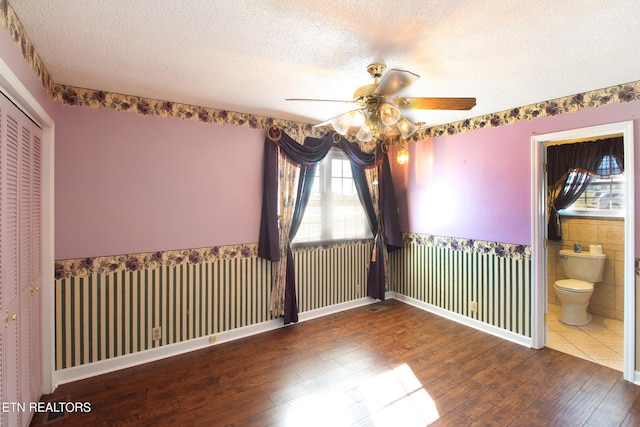 empty room featuring hardwood / wood-style flooring, a ceiling fan, a textured ceiling, and a wainscoted wall